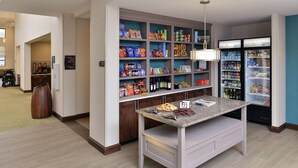 Un hall de hotel con una barra de aperitivos autoservicio, un refrigerador y una máquina de café.
