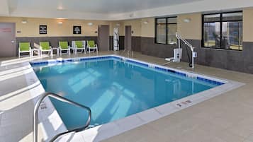 Una piscina interior con un puesto de socorrista, una escalera de piscina y un cartel de prohibido bucear.