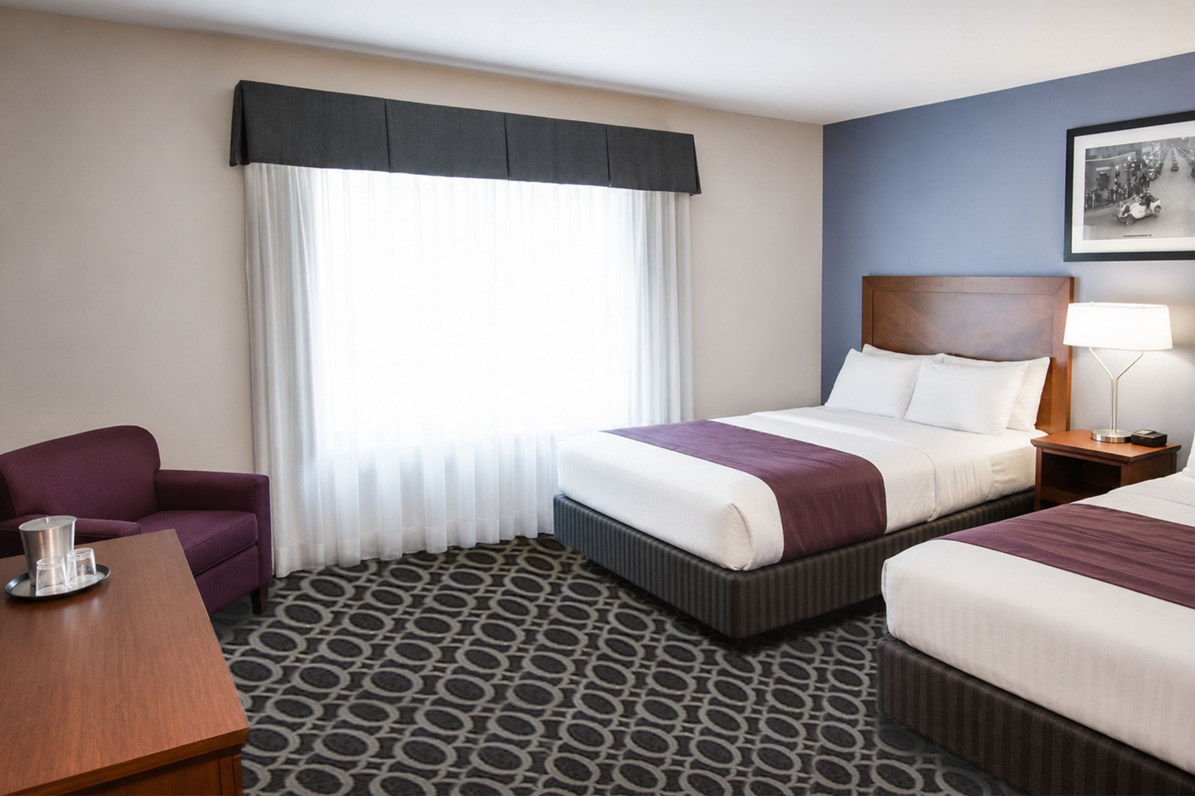 A hotel room with a bed, a chair, a bedside table, a lamp, and a window with curtains.