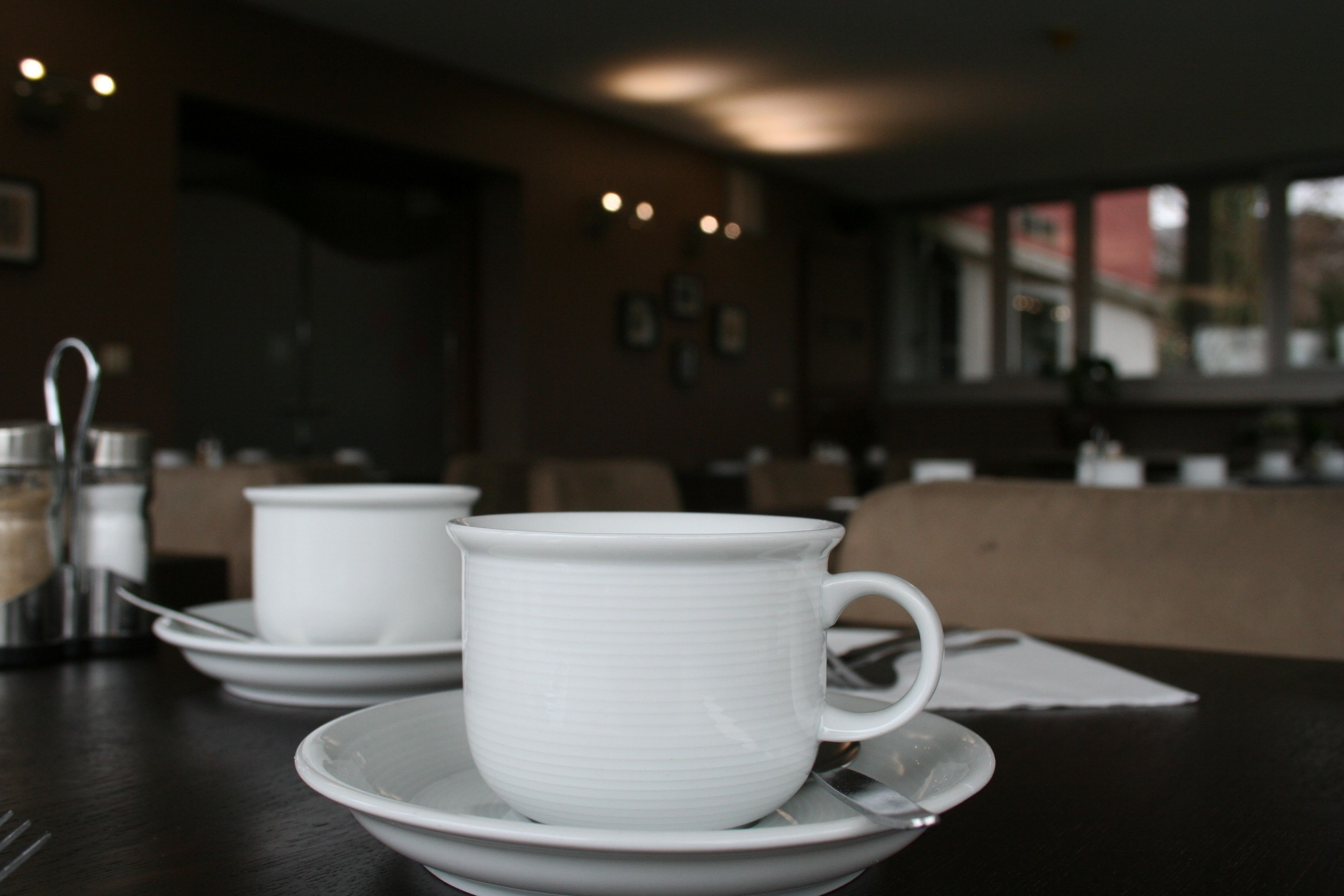 A table with a white cup and saucer, a spoon, and a salt shaker.