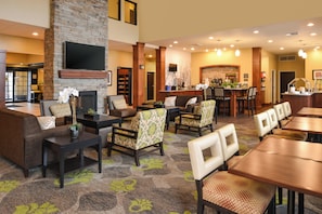 A hotel lobby with a fireplace, seating area, bar, and a television mounted on the wall. - Staybridge Suites Merrillville by IHG (Merrillville)