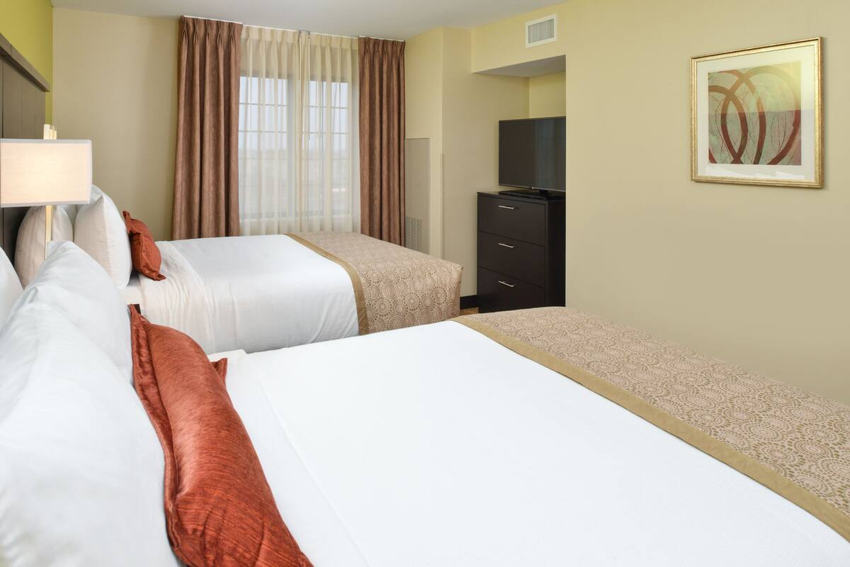 A hotel room with two beds, a TV, a dresser, and a painting on the wall.