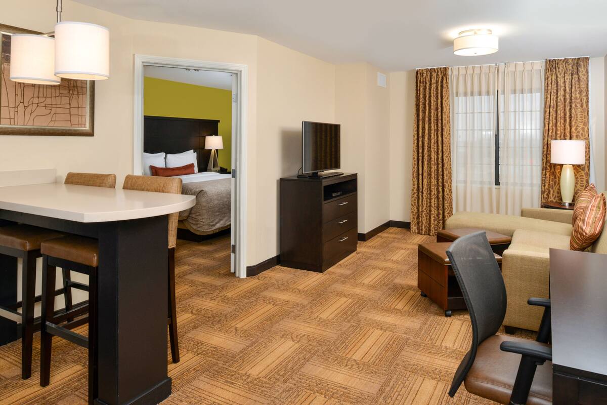 A hotel room with a dining area, a sofa, a TV, and a desk.