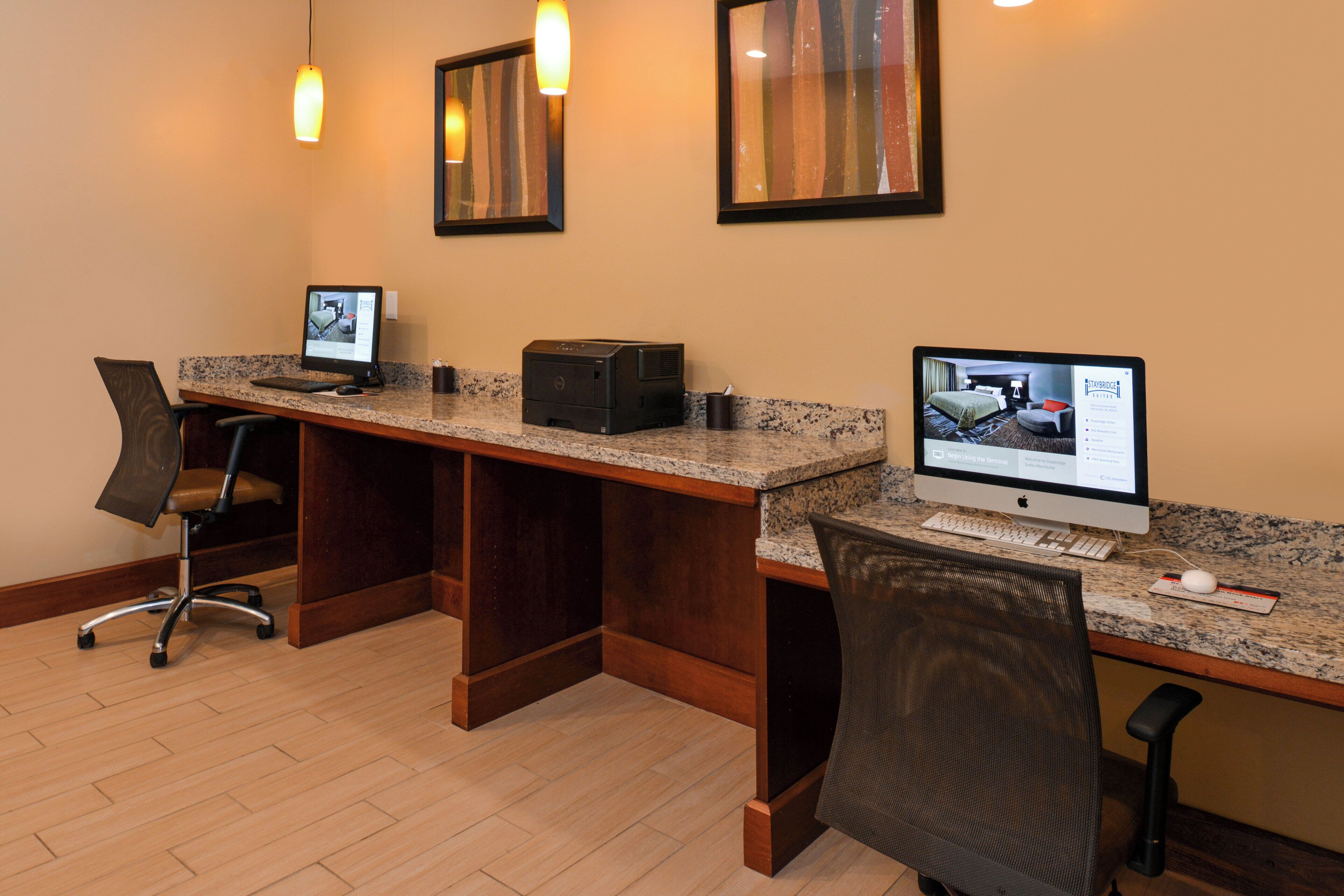 A hotel room with a desk, two computers, a chair, and a bed.