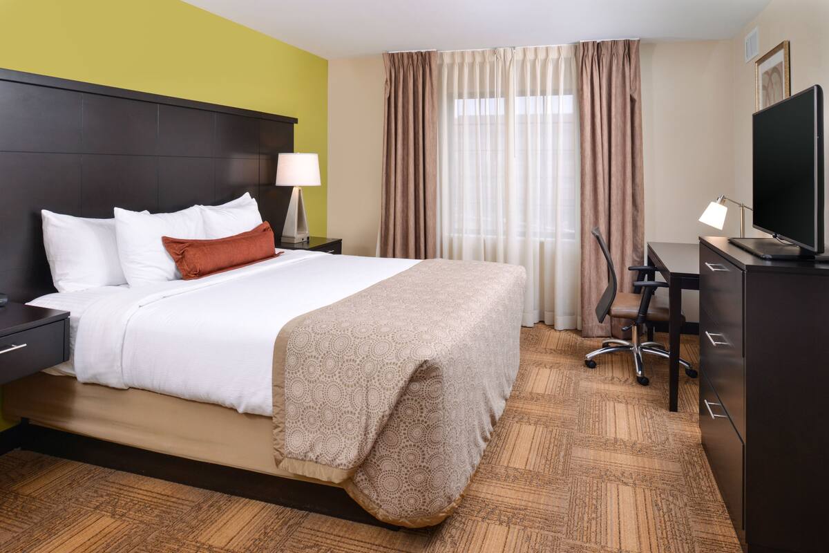 A hotel room with a bed, a desk, a chair, a TV, and a lamp.