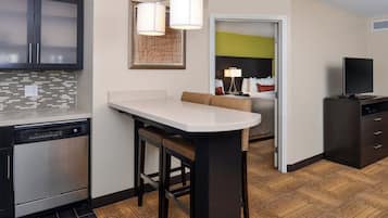 A modern kitchen with a built-in dishwasher, a dining area with a bar stool, and a living space with a sofa and a television.