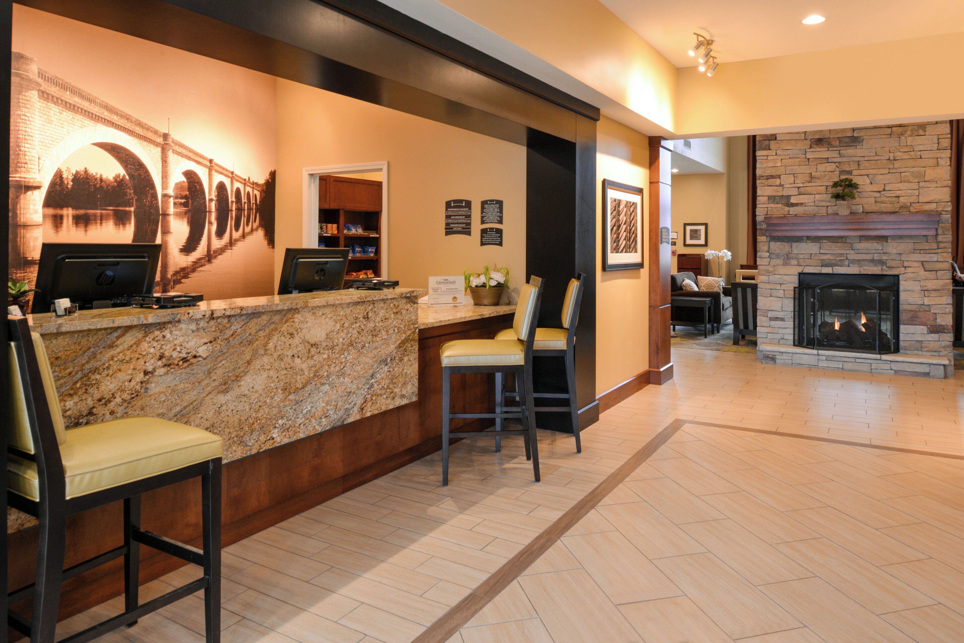A reception area with a marble counter, two bar stools, a fireplace, and a stone wall.