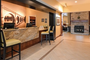 A reception area with a marble counter, two bar stools, a fireplace, and a stone wall. - Staybridge Suites Merrillville by IHG (Merrillville)