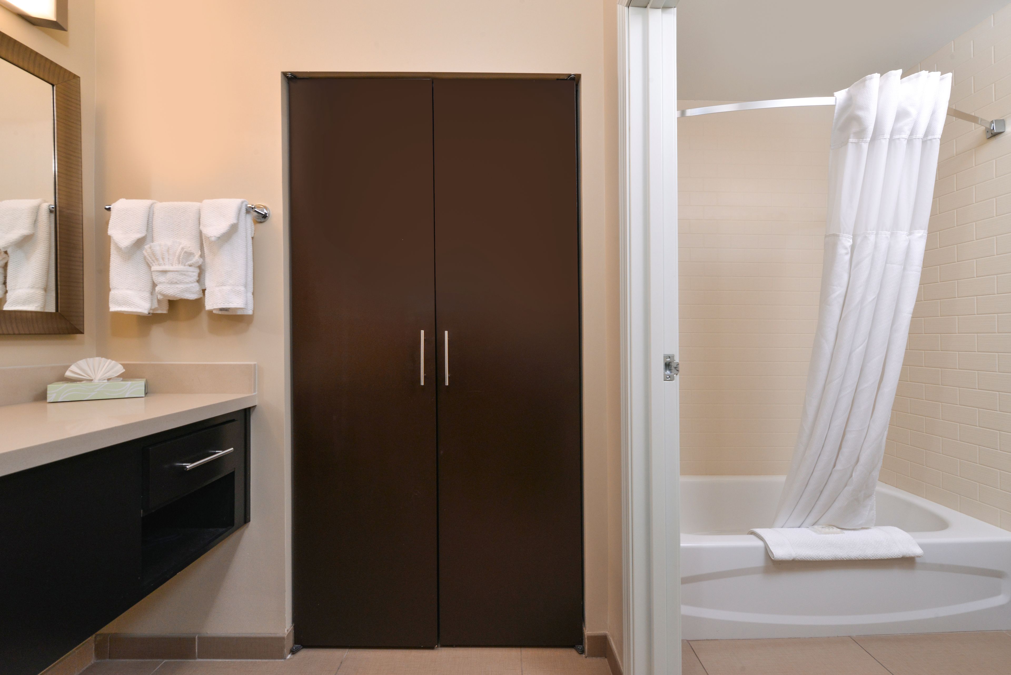 A bathroom with a dark brown wardrobe, a white bathtub, and a white shower curtain.