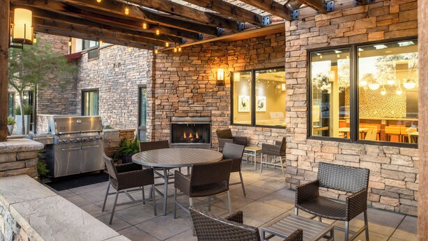 An outdoor patio with stone walls, a grill, a fireplace, and wicker furniture. - TownePlace Suites by Marriott Lancaster, CA (Lancaster)