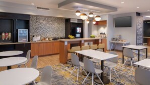 A modern kitchen area with a refrigerator, microwave, and coffee machine. There are tables and chairs arranged for dining. - TownePlace Suites by Marriott Lancaster, CA (Lancaster)