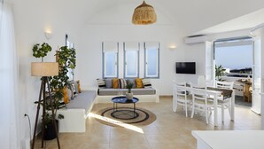 Ein modernes Wohnzimmer mit Sofa, Esstisch und Stühlen, großen Fenstern und Meerblick.