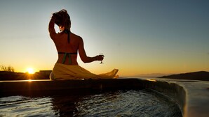 Eine Person sitzt am Wasser bei Sonnenuntergang.