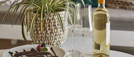 A dining table with a plate of chocolate-covered strawberries, a bottle of white wine, and two wine glasses.