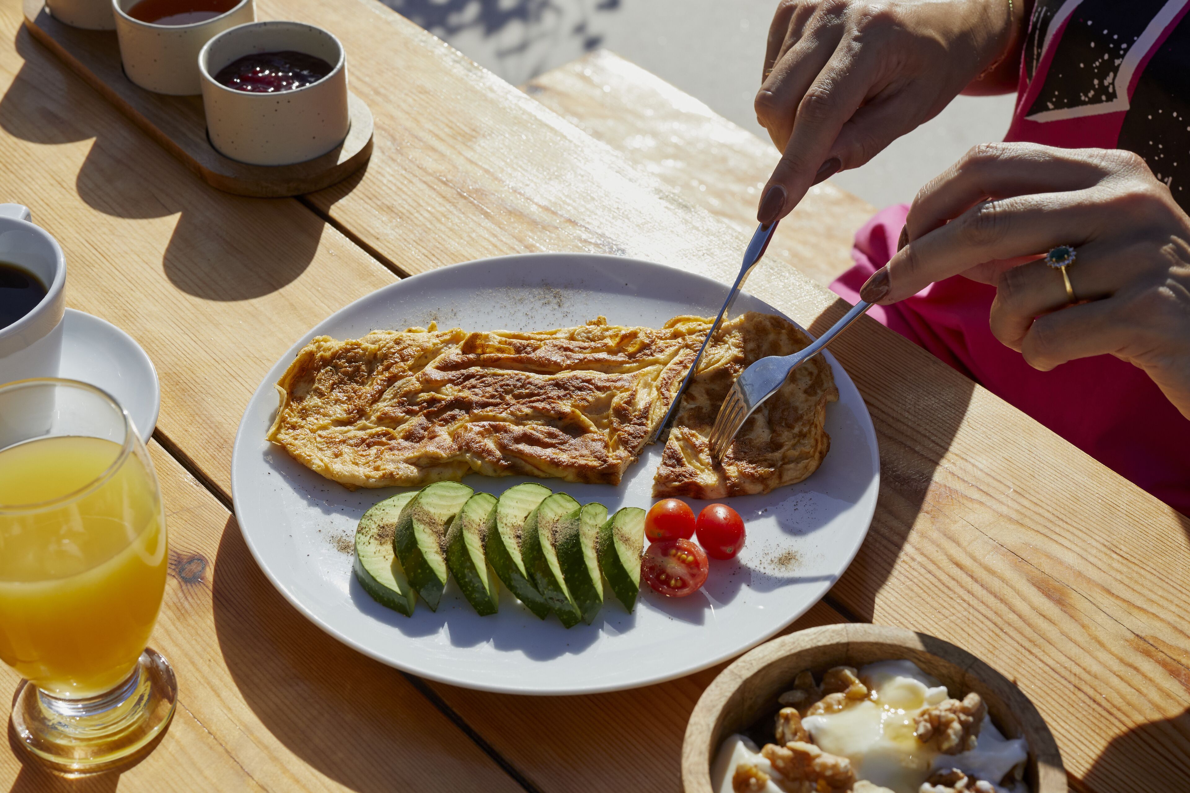 Un plato de desayuno con una rebanada de tostada, rodajas de aguacate, tomates cherry y un tazón pequeño de nueces.