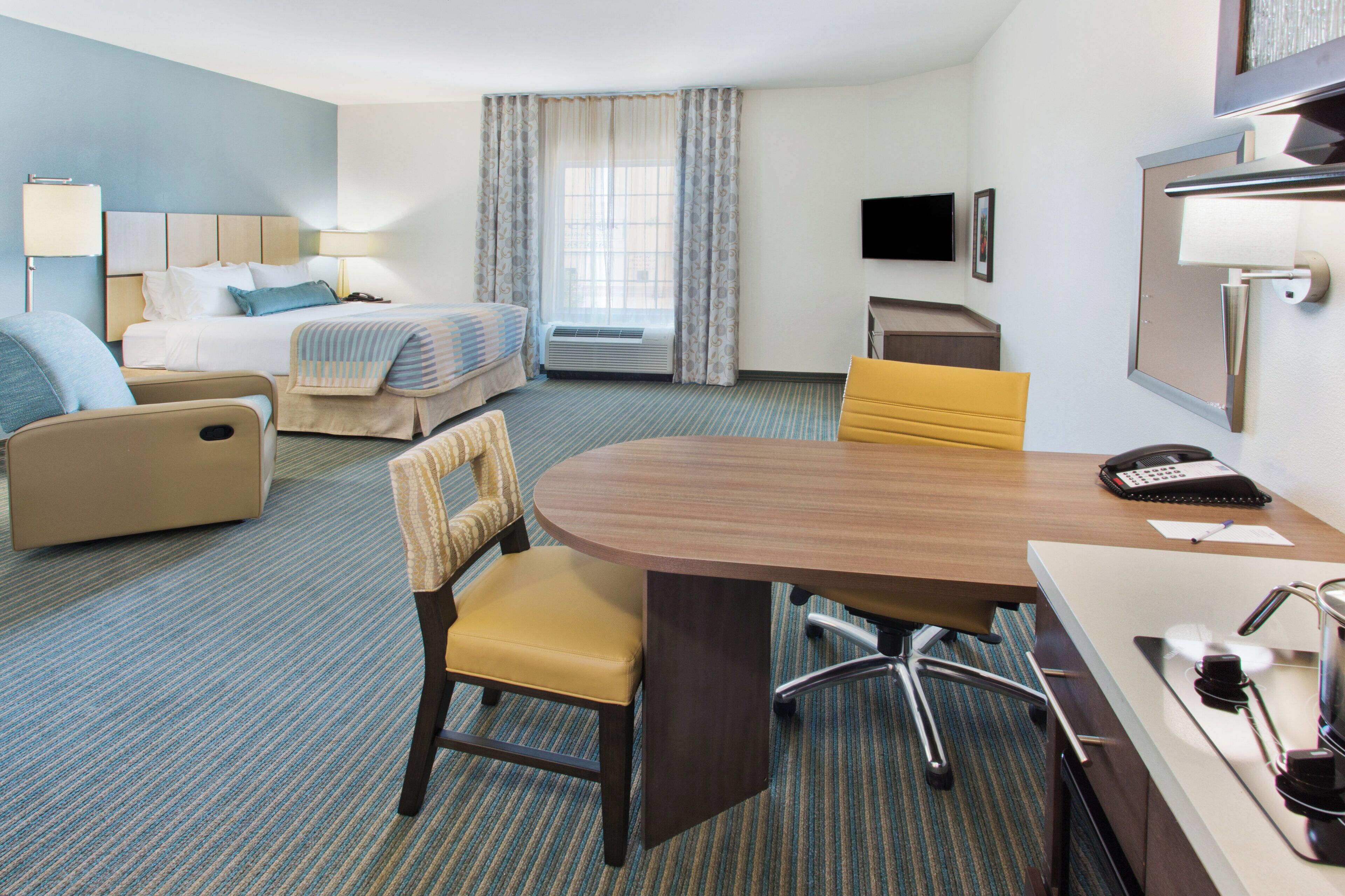 A hotel room with a bed, a desk with a chair, a TV, and a window with curtains.