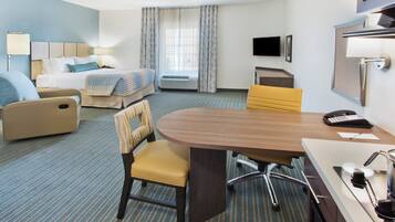 A hotel room with a bed, a desk with a chair, a TV, and a window with curtains.