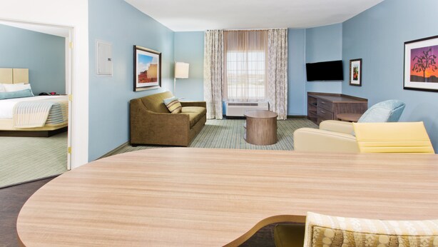 Una habitación de hotel con una amplia mesa de madera, un sofá, una silla, una cama, un televisor y una ventana con cortinas.