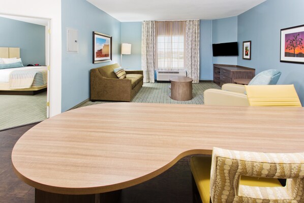 Een hotelkamer met een grote houten tafel, een bank, een stoel, een bed, een televisie en een raam met gordijnen.