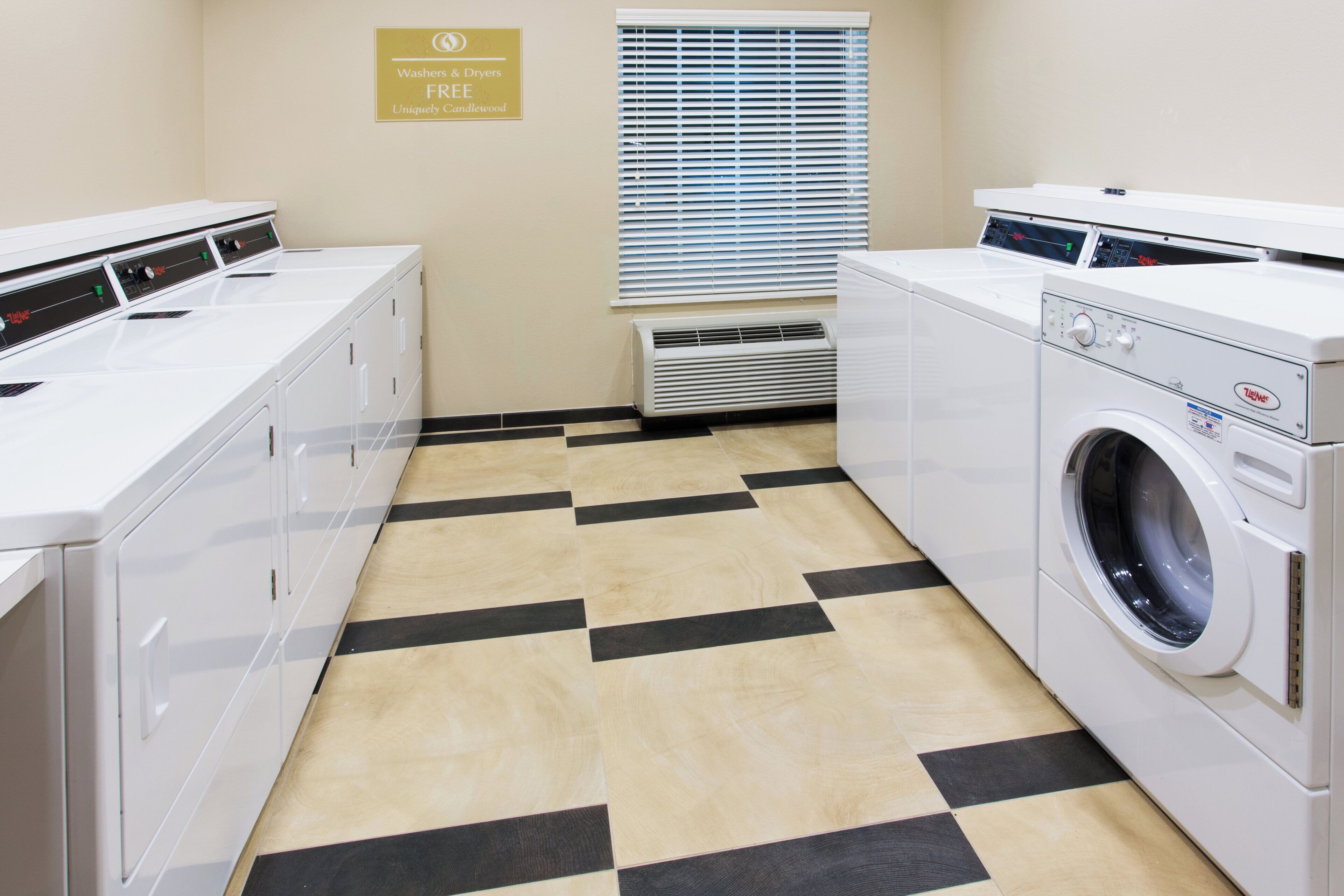 A laundry room with a checkered floor, a sign indicating free washers and dryers, and a window with blinds.