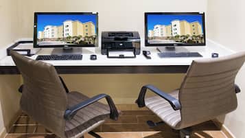 A desk with two monitors, a printer, and a keyboard. There are two office chairs.