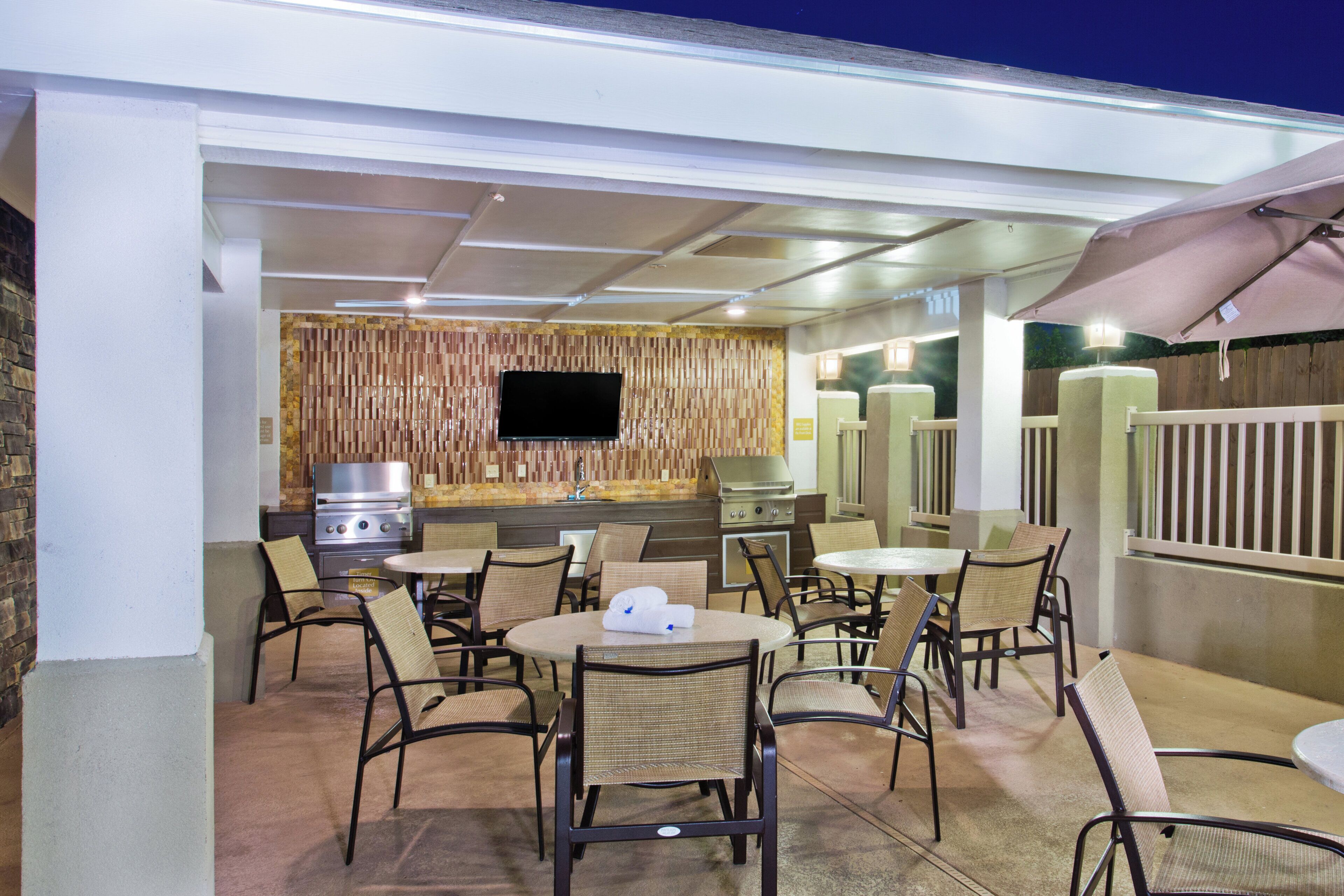 An outdoor patio area with seating, a grill, and a flat-screen TV.