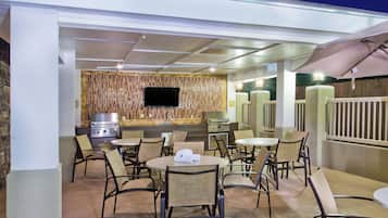 Un espacio de patio al aire libre con asientos, una parrilla y un televisor de pantalla plana.
