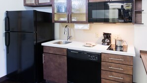 Una cocina compacta equipada con refrigerador, lavavajillas, microondas y cafetera.