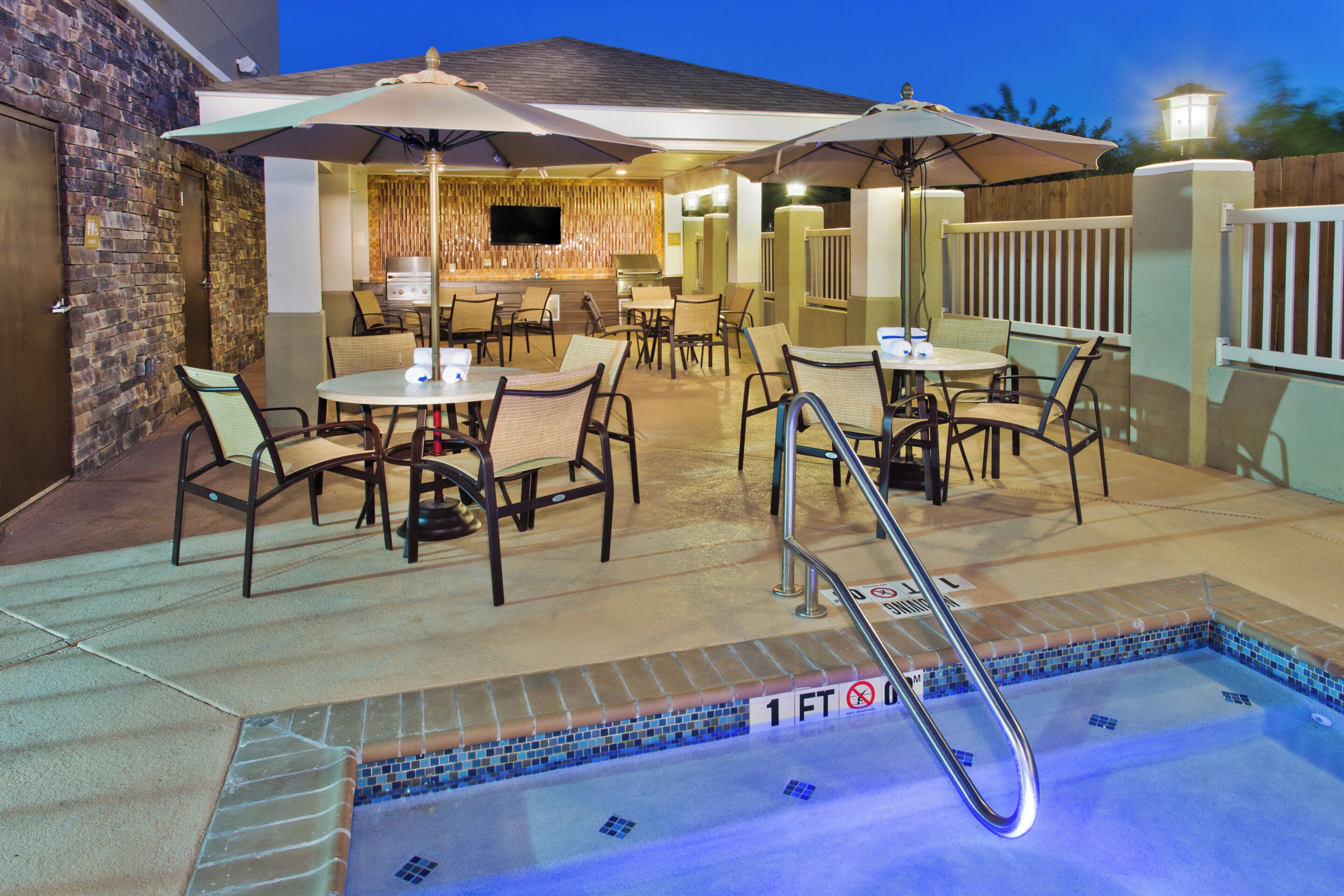 An outdoor pool area with a hot tub, seating, and umbrellas.