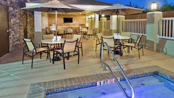 An outdoor pool area with a hot tub, seating, and umbrellas.