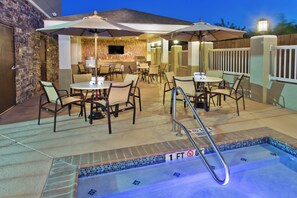 Zona de piscina exterior con jacuzzi, asientos y sombrillas.
