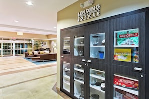 A modern hotel lobby with a lending locker area, a seating area with sofas, and a clear view of the exit. - Candlewood Suites Corpus Christi-Naval Base Area by IHG (Corpus Christi)