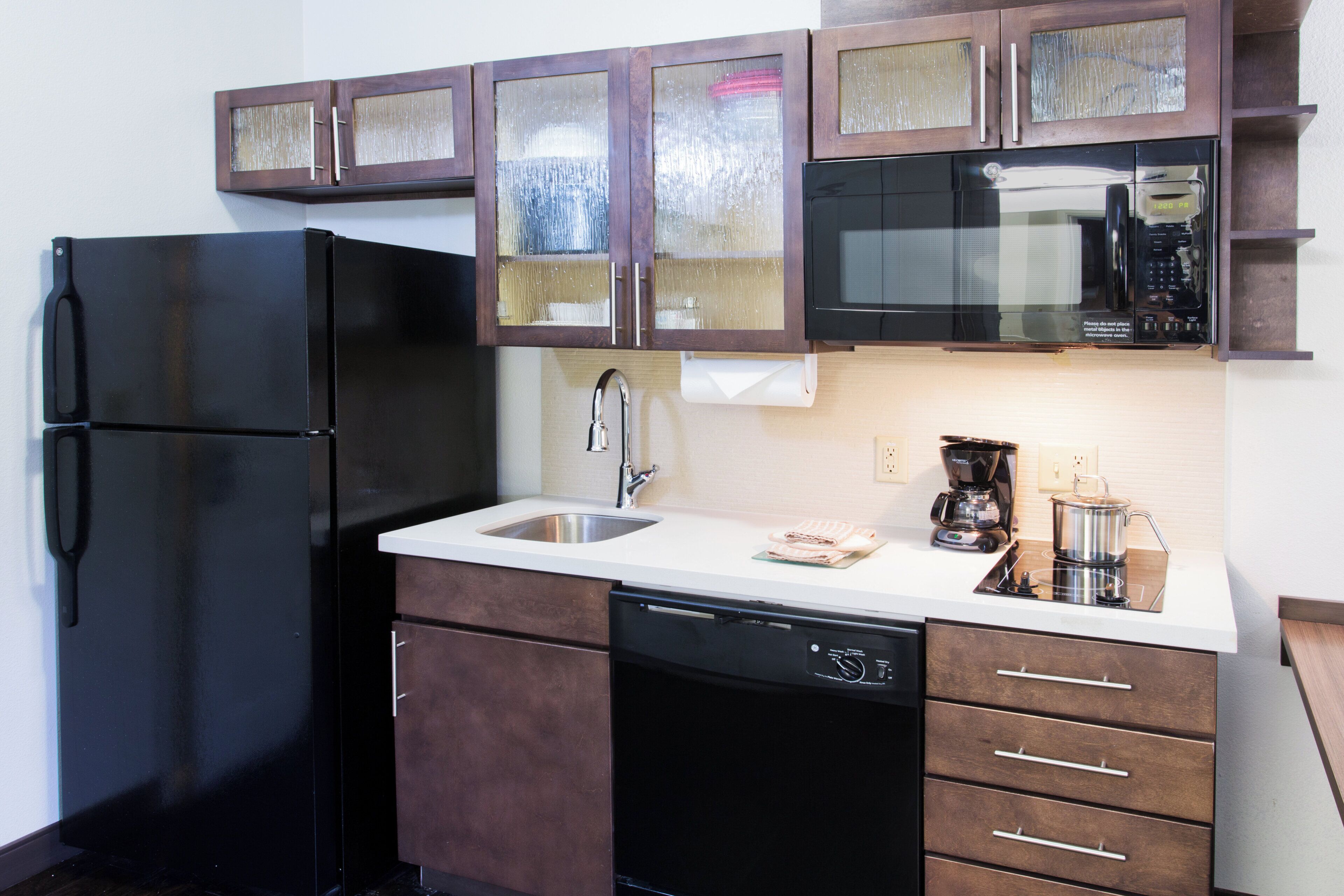 Una cocina compacta con un refrigerador negro, un microondas y una cafetera sobre la encimera.