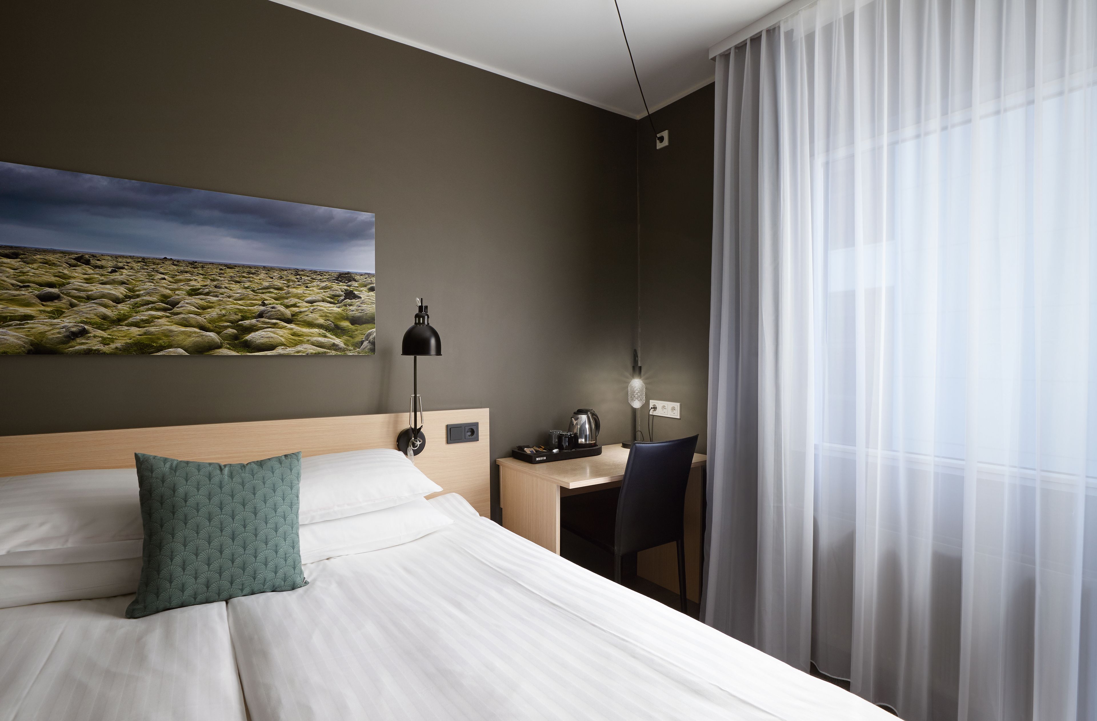 Una habitación de hotel con una cama, un escritorio, una silla, una lámpara y un cuadro en la pared.