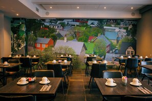 Un restaurante con mesas listas para comer, un mural de casas al fondo y vistas del entorno.