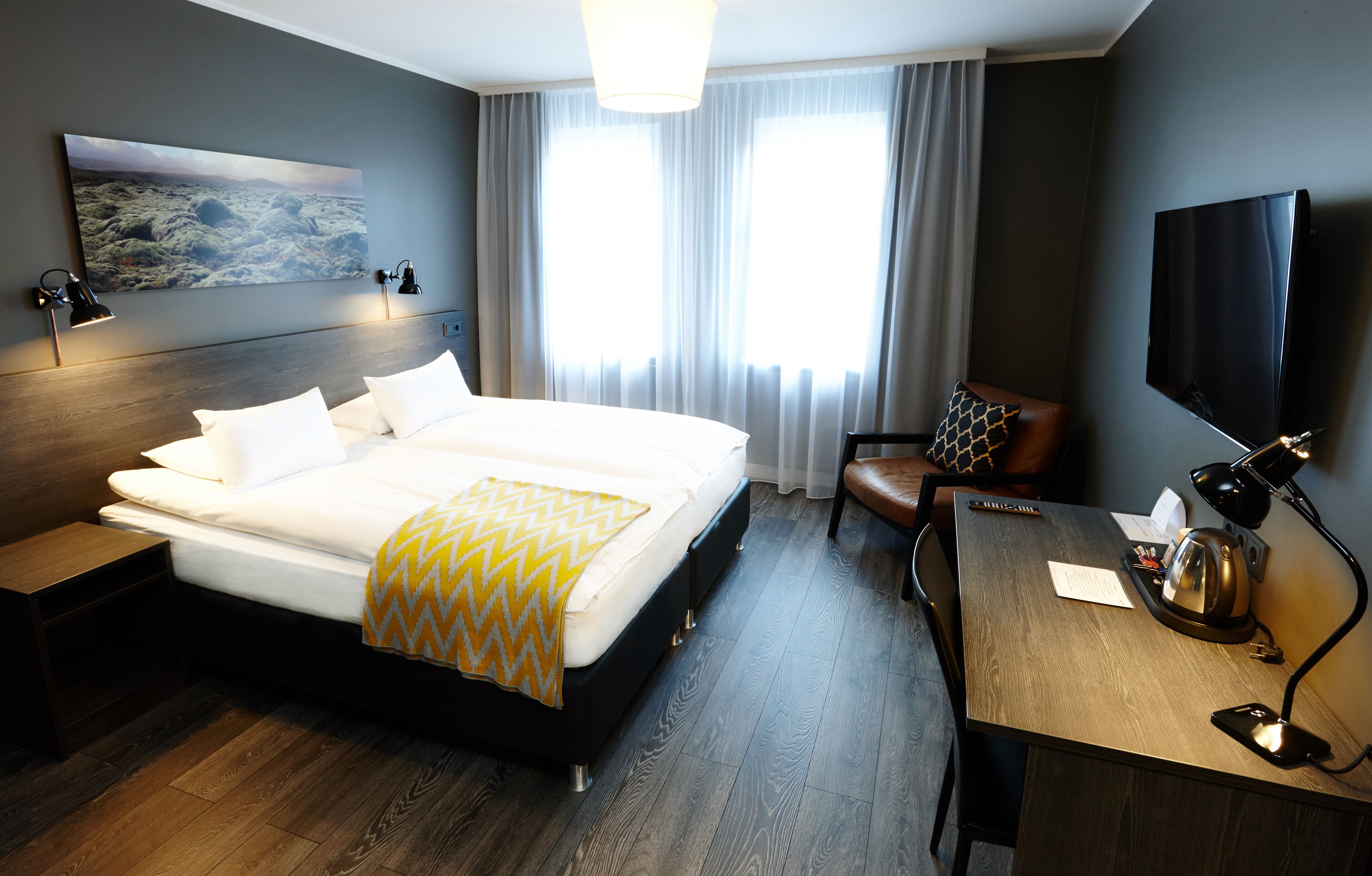 A hotel room with a large bed, a desk with a chair, a TV, and a painting on the wall.
