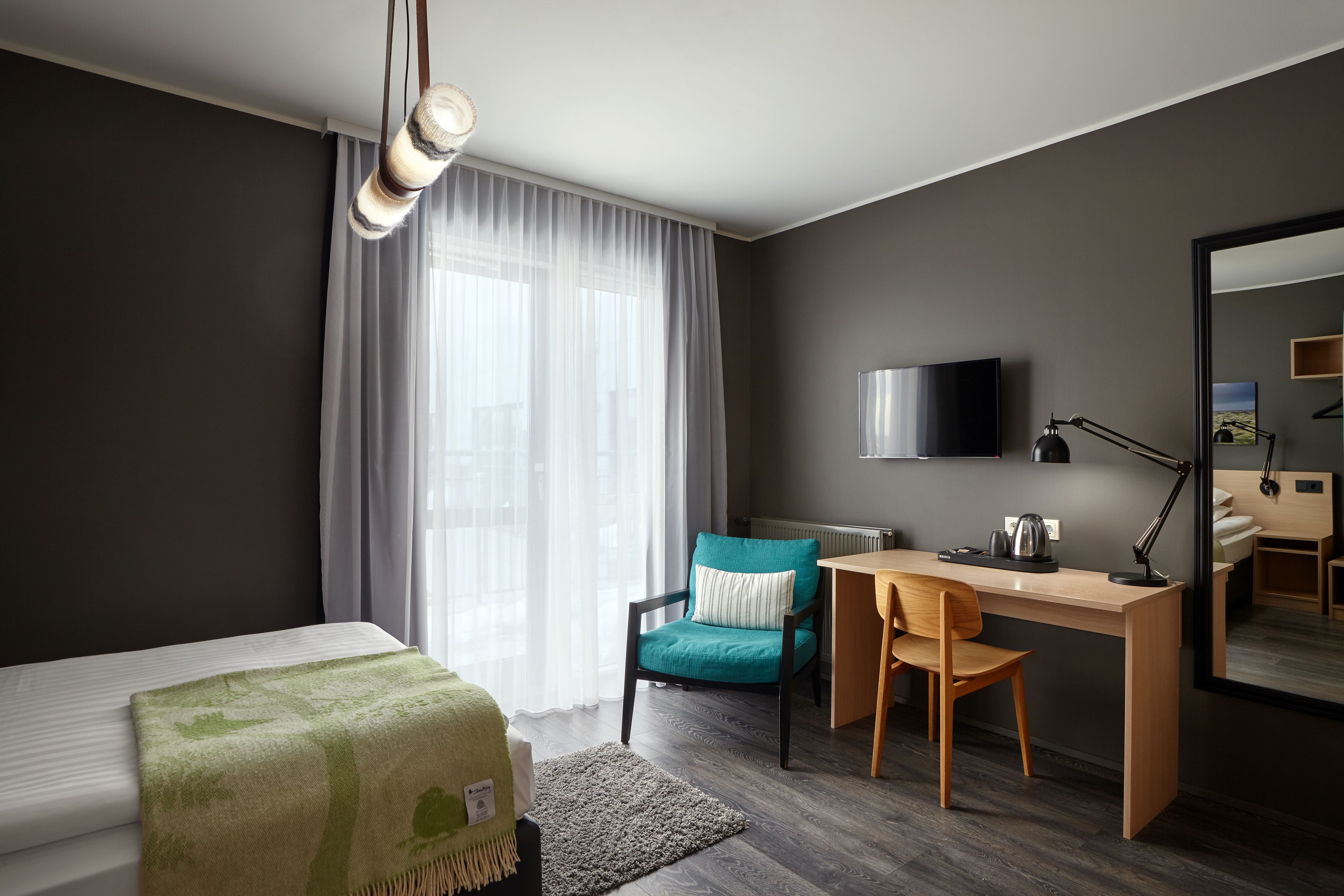 A modern hotel room with a bed, a desk, a chair, a television, and a large mirror.