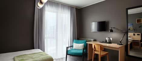 A modern hotel room with a bed, a desk, a chair, a television, and a large mirror.
