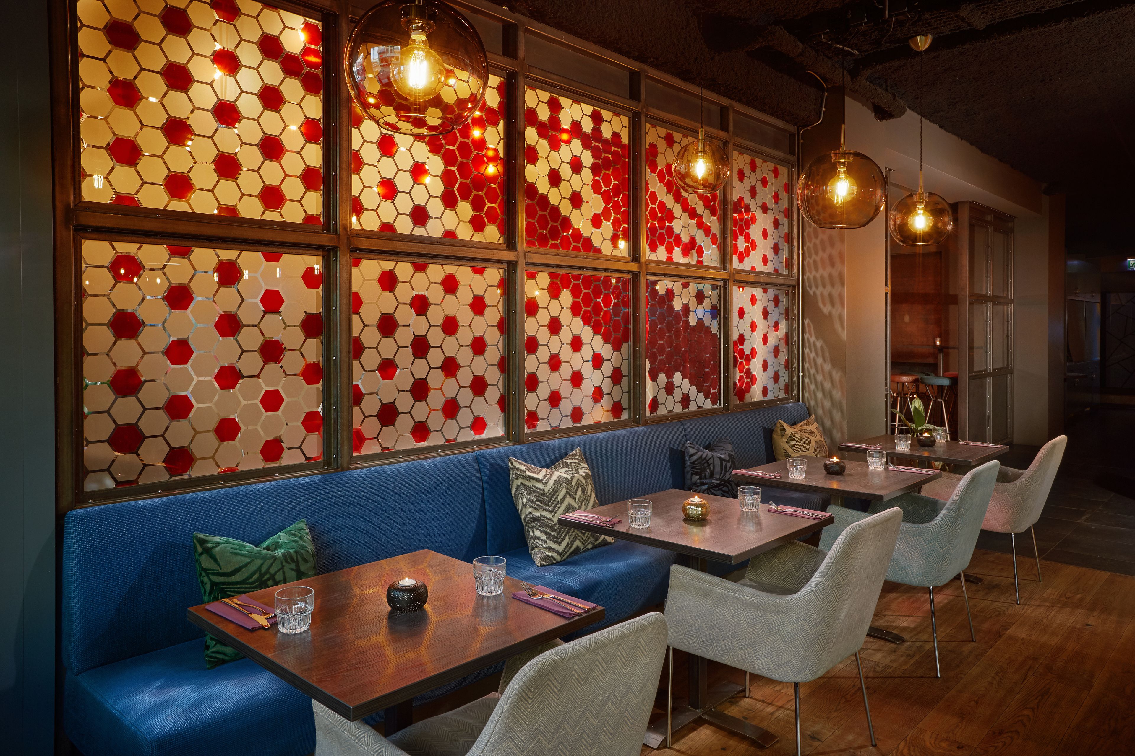 A restaurant with hexagonal patterned windows, wooden tables, and upholstered seating.