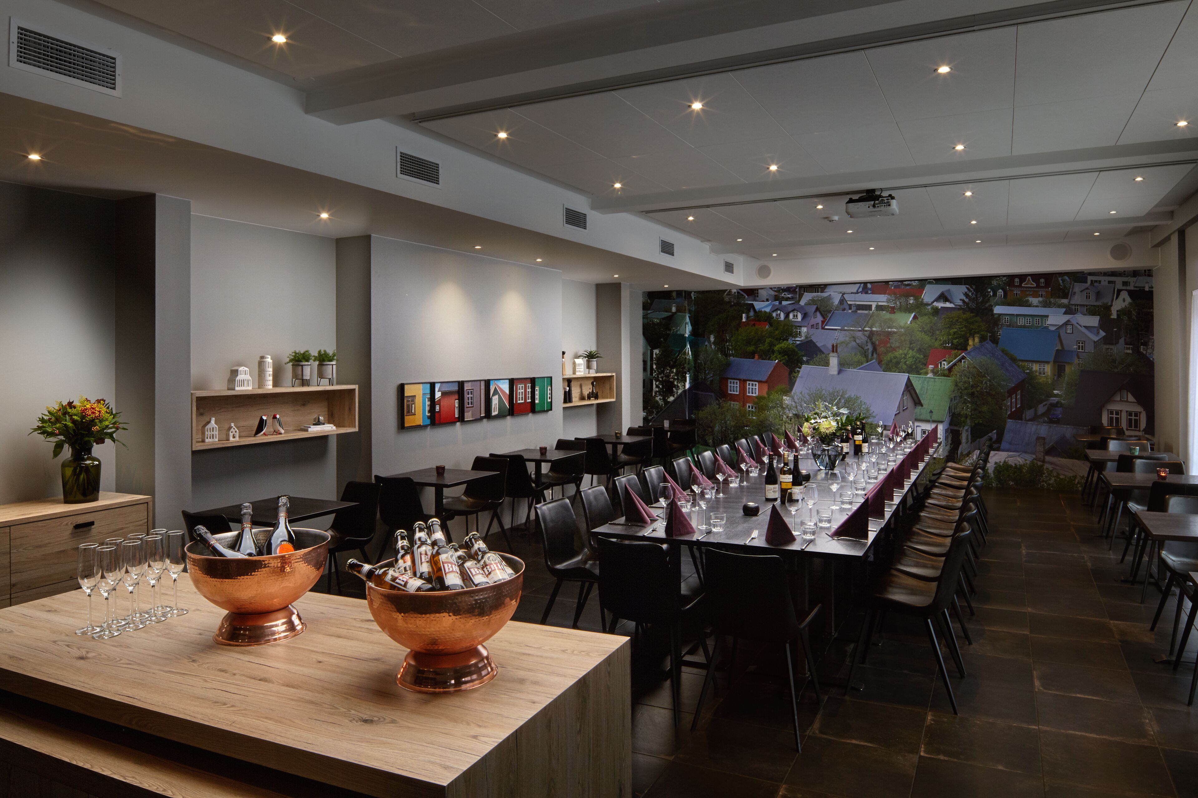 A restaurant with a long dining table, multiple chairs, and a bar area with copper buckets of bottles.