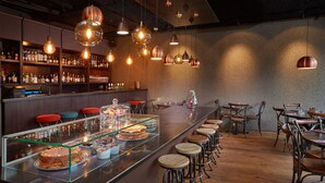 Una zona de bar con una barra alargada, taburetes y lámparas colgantes.