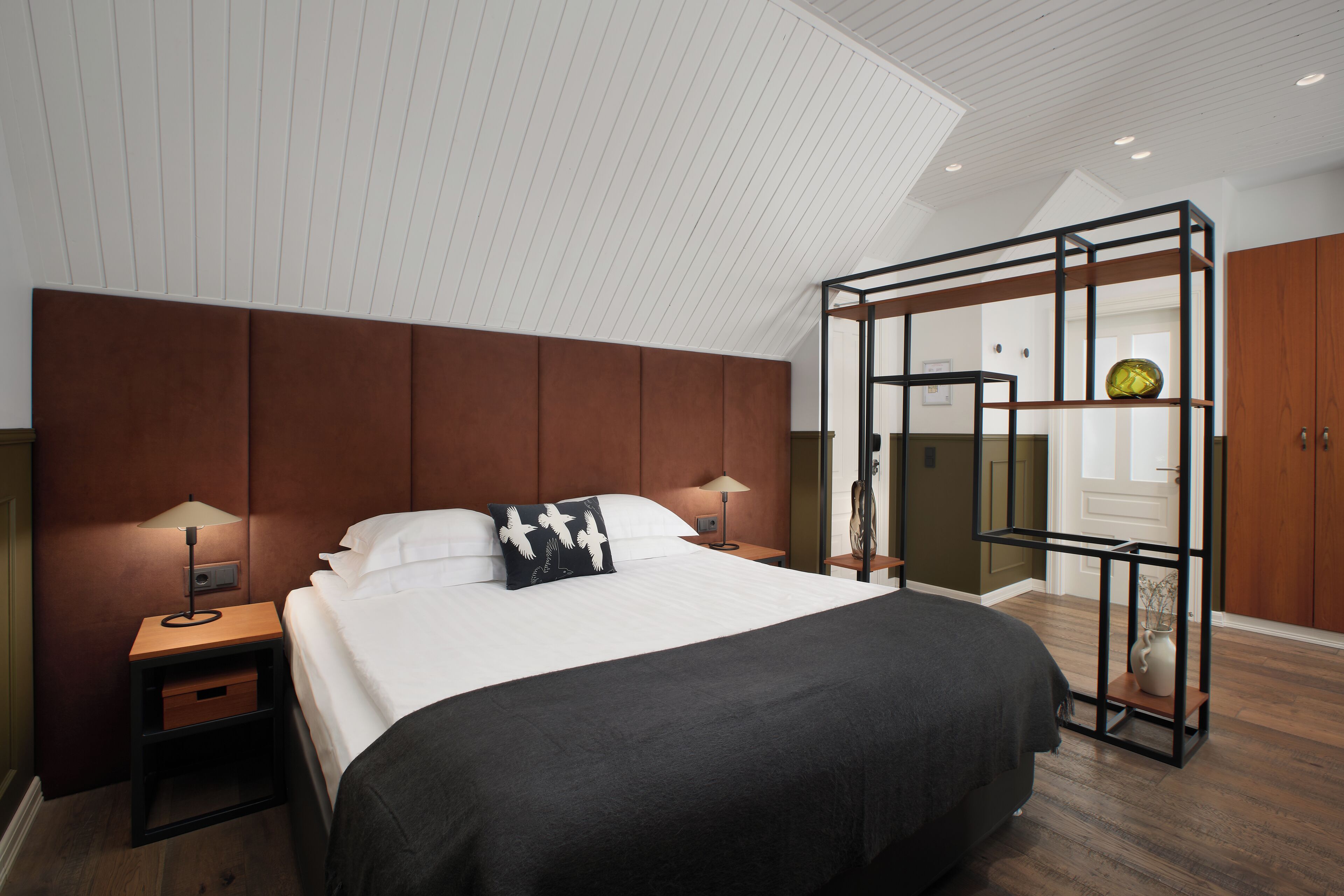 A modern hotel room with a large bed, wooden headboard, and a unique glass partition.