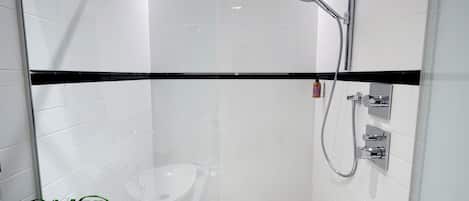 A modern bathroom with white tiles, a black accent strip, a glass shower enclosure, and a handheld showerhead.