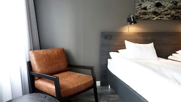 A modern hotel room with a single bed, a brown leather chair, a round table, and a wall-mounted lamp.