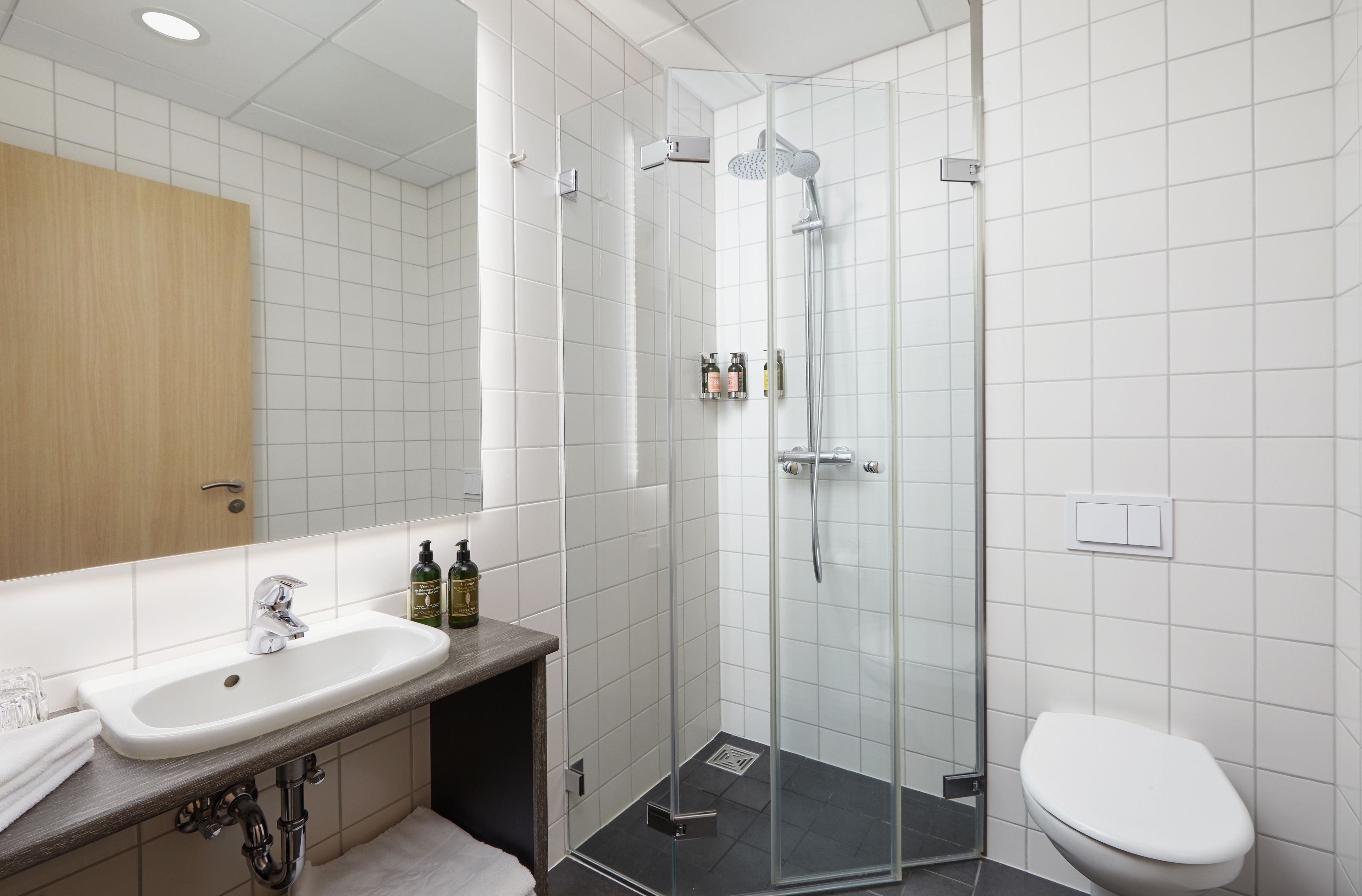 Une salle de bain moderne avec une douche à parois de verre, un lavabo doté d’un plan de travail en bois et des toilettes.