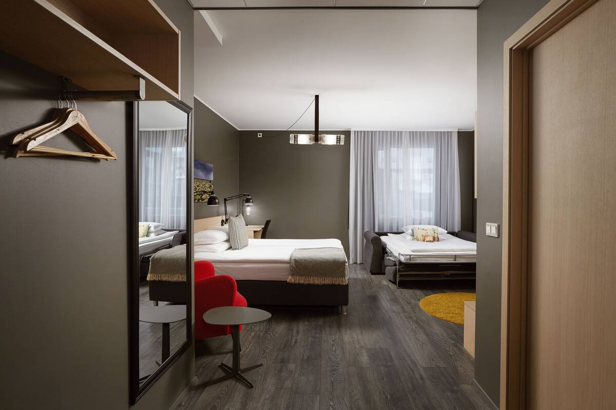 A modern hotel room with a bed, a desk, a chair, a mirror, and a small table.