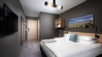 A modern hotel room with a large bed, a flat-screen TV, a painting, and a wooden headboard.