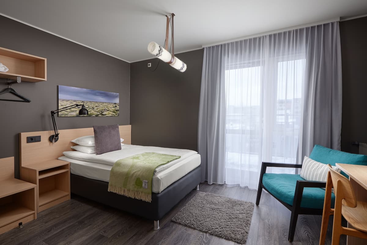 A modern bedroom with a bed, bedside tables, a desk, a chair, a hanging lamp, and a window with curtains.
