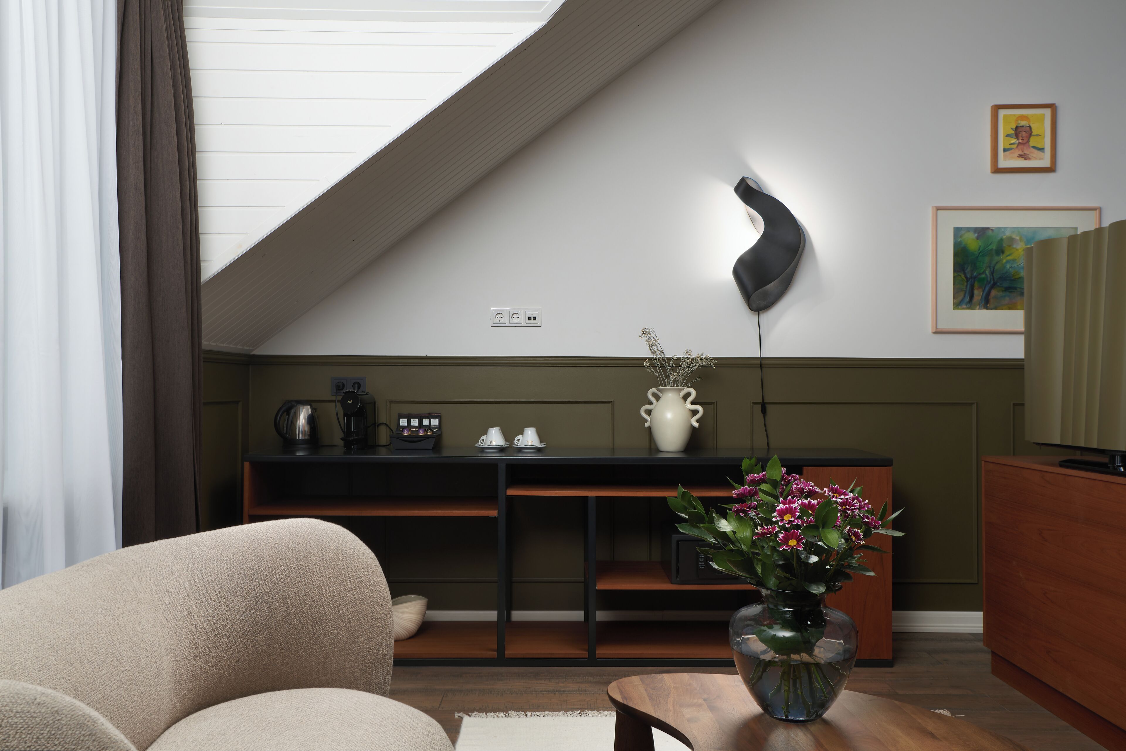A modern living room with a curved ceiling, a sofa, a coffee table, a vase with flowers, a desk with a lamp, and artwork on the wall.