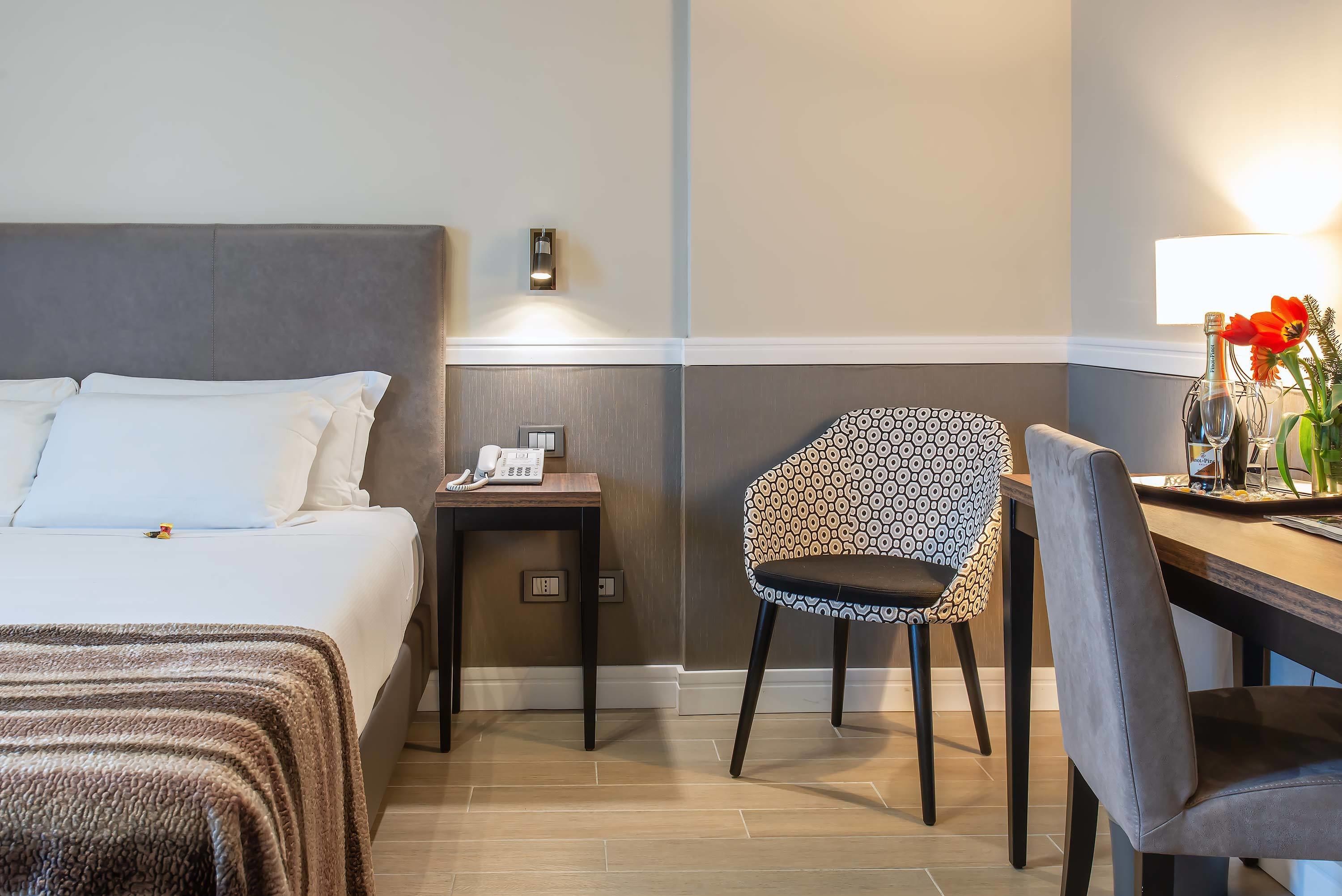 Habitación de hotel con cama, escritorio, silla, teléfono y lámpara de pared.